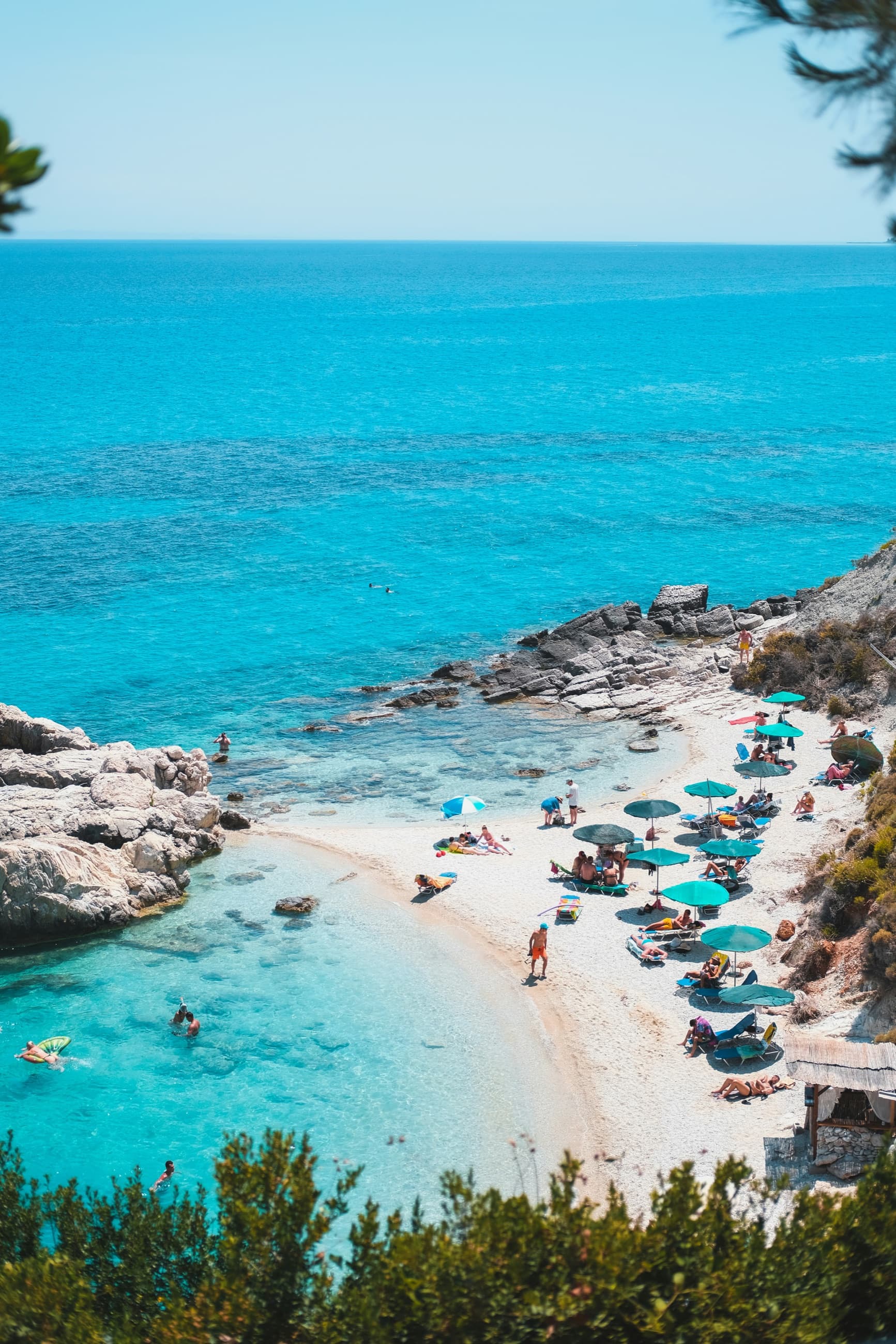 A turquoise cove with umbrellas on a white pebble beach in Greece