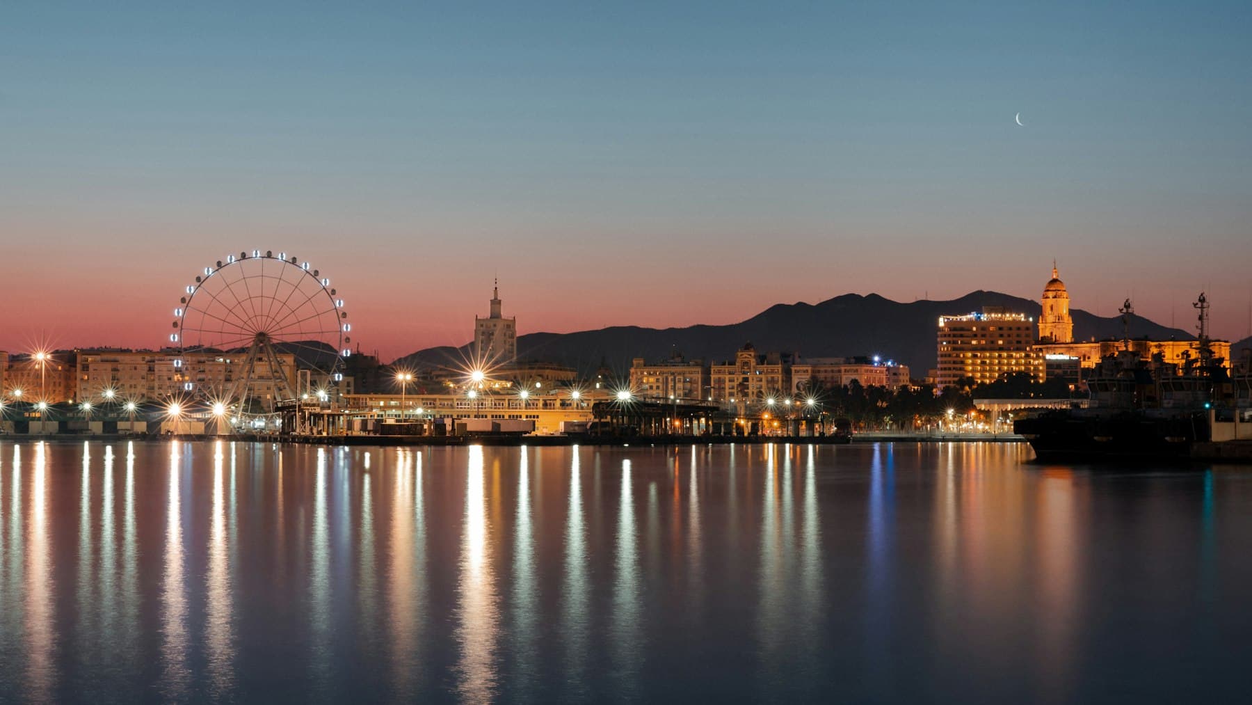 Málaga waterfront at blue hour, city lights reflecting across the harbour